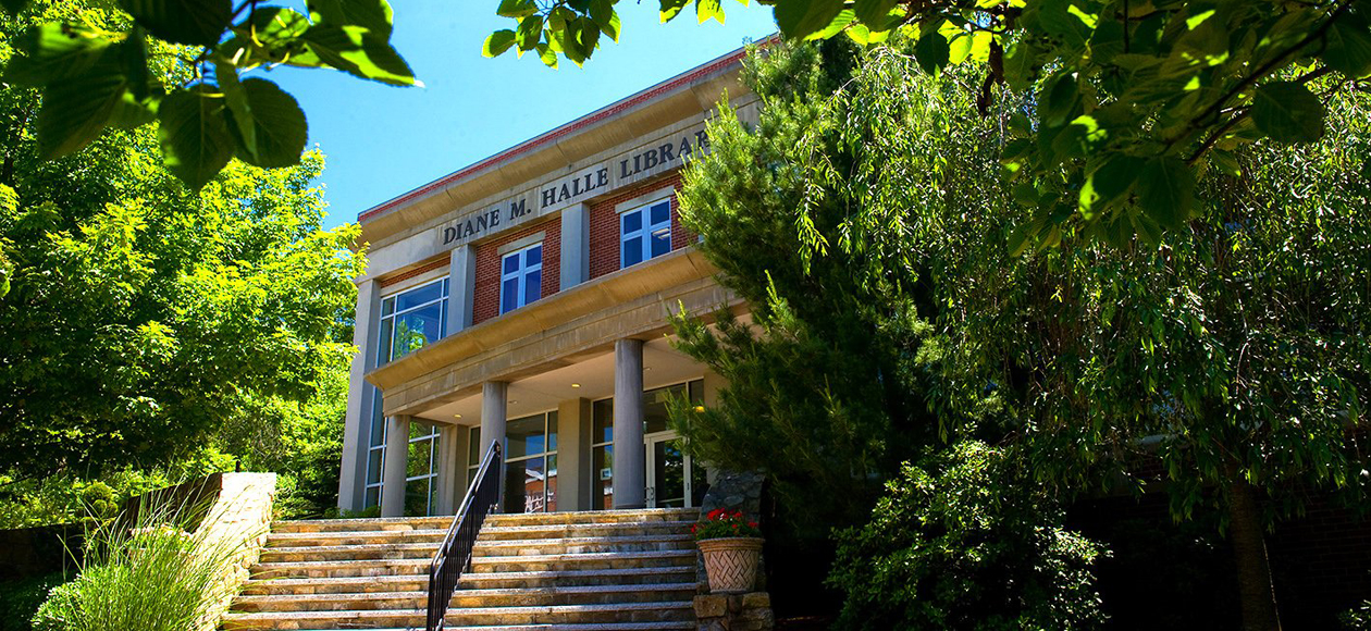 This is an image of the Diane M. Halle Library on the campus of Endicott College. This is a view of the library with some greenery peeking through the top of the photo on a bright day.