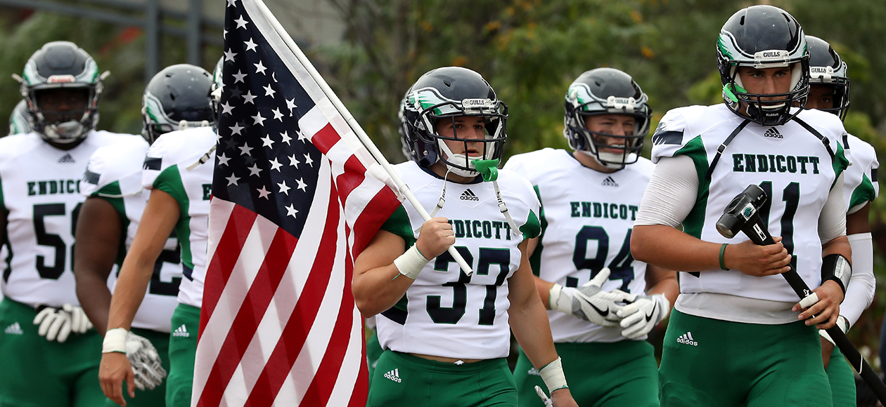 The Endicott football team enters the field with an American Flag.