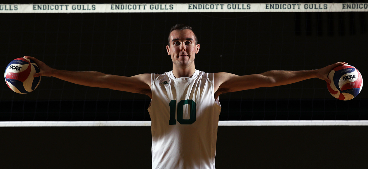 Matt Bozek poses with volleyballs near a net.