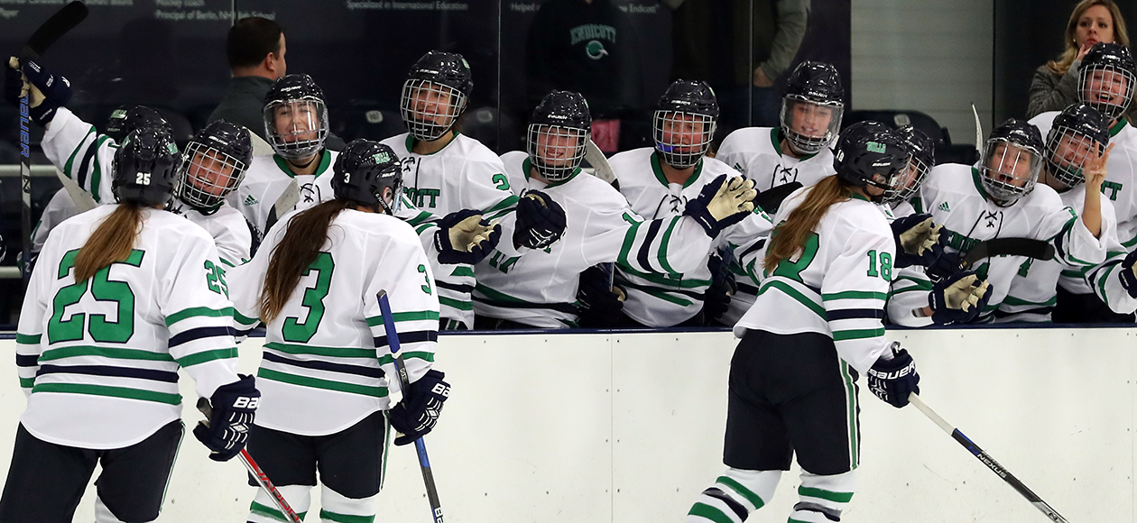 The women's ice hockey bench high fives teammates on the ice after a goal. 