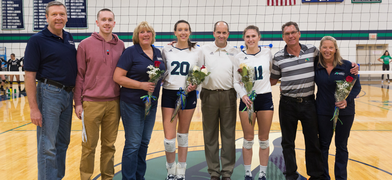 Image of seniors Emily Diezmann and Emma Mancini posing at the net with head coach Tim Byram and their families.