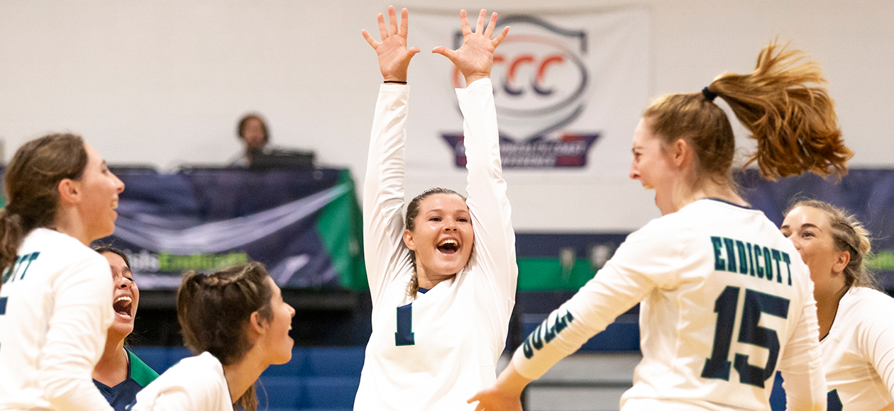 Image of the women's volleyball starters celebrating a kill by Krystina Schueler, as Amanda Gilbert has both arms outstretched above her head.
