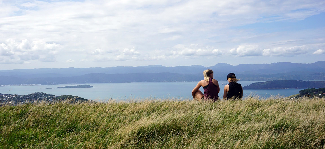 Bridget Cott and a friend sitting on a cliff in New Zealand.