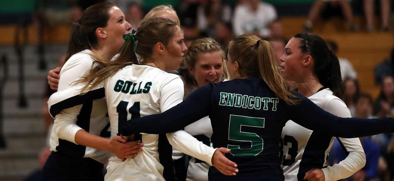 Image of the women's volleyball team bringing it together on the court after winning a point.