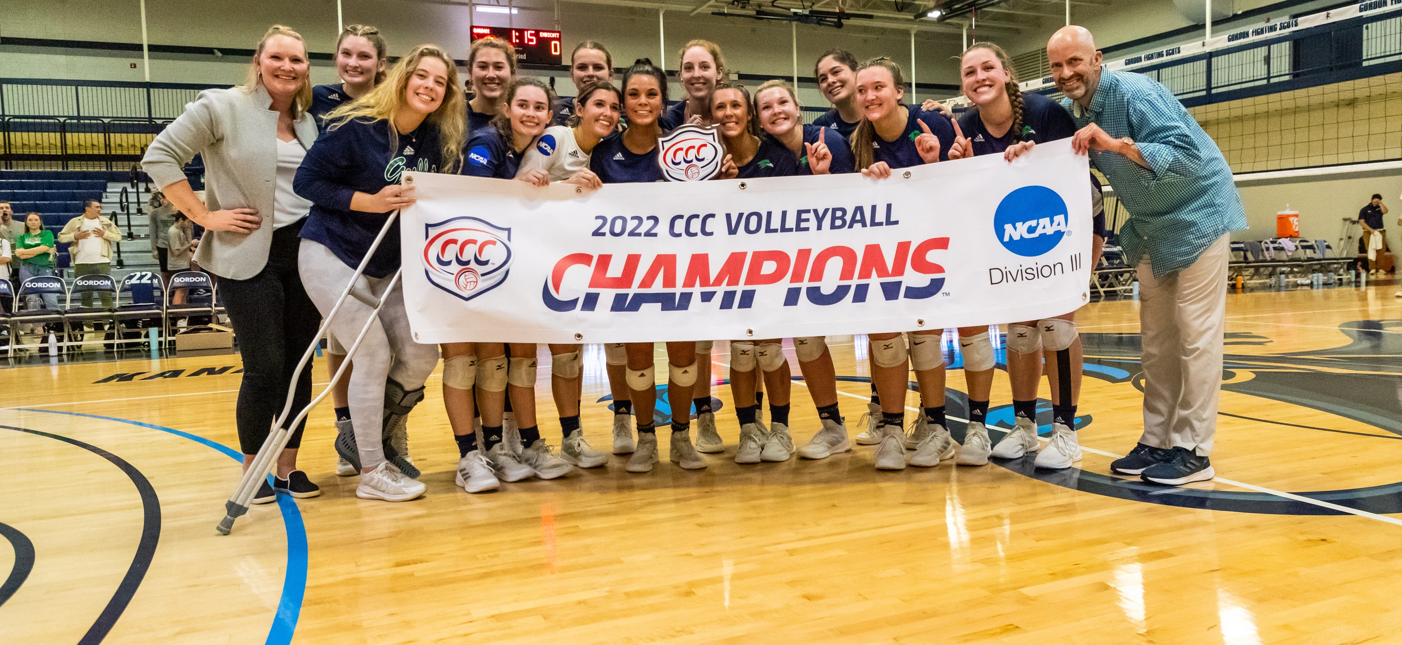 The women's volleyball team and coaching staff poses with the CCC trophy and banner on Gordon's court.