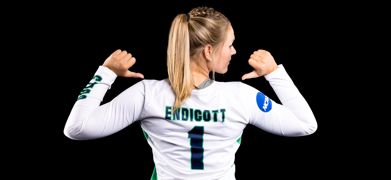 Image of Amanda Gilbert, back facing the camera, with her head turned to the side, and both arms up with her thumbs pointing at Endicott across her shoulders.